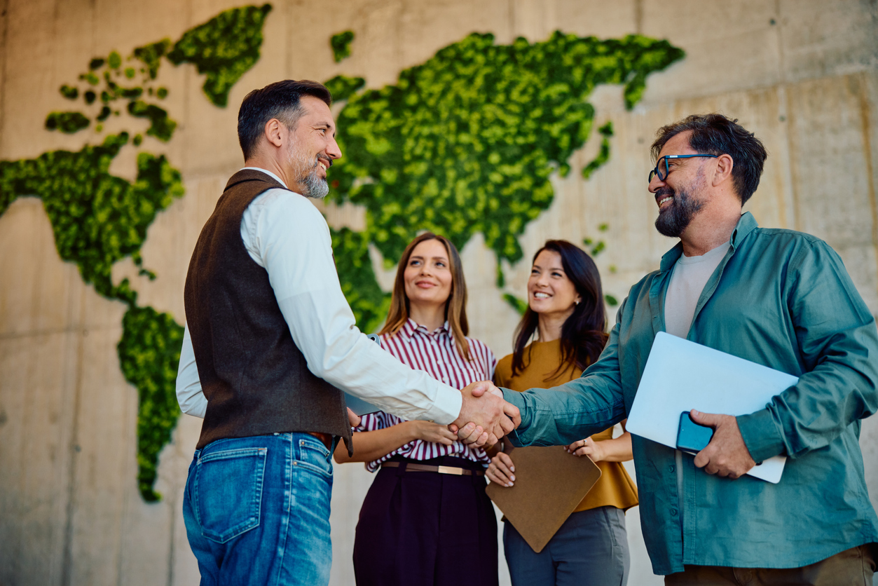 Business-Team bei Händedruck vor grüner Weltkarte - Persönliche Betreuung SINA Marketing GmbH